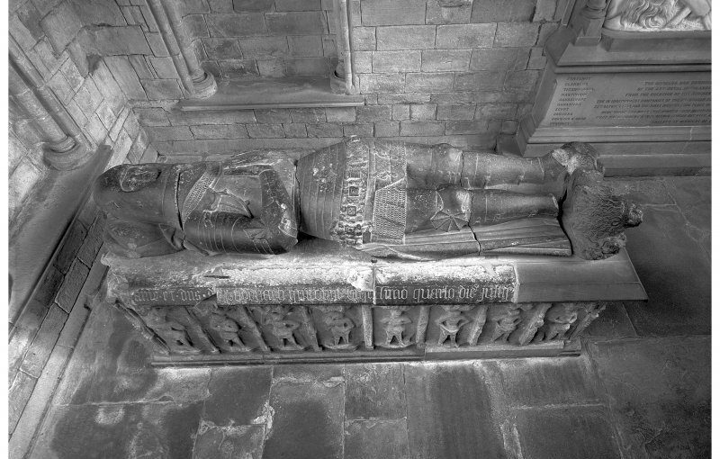 Black and white photo looking down from upon high of a stone tomb with a knighted figure in armour lying on top